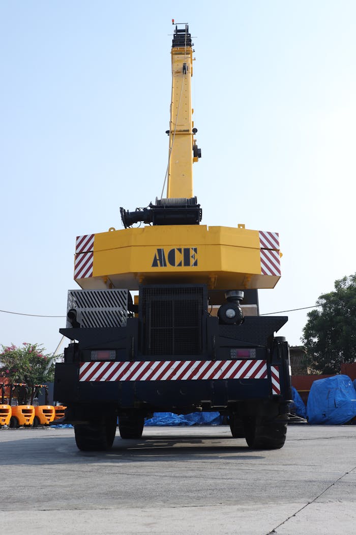 Yellow ACE crane in a construction yard in Faridabad, India with clear blue sky.