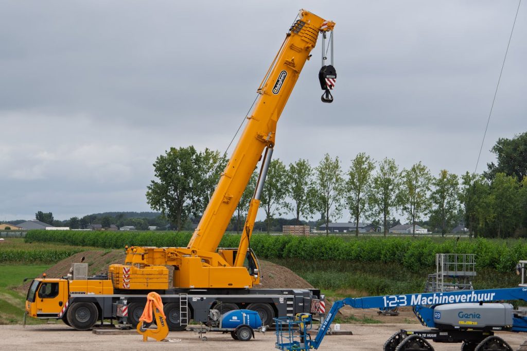 Doğru Vinç Seçimi: Projenizin Başarısı İçin Anahtar Kriterler A large yellow crane at a construction site with lush greenery in the background.